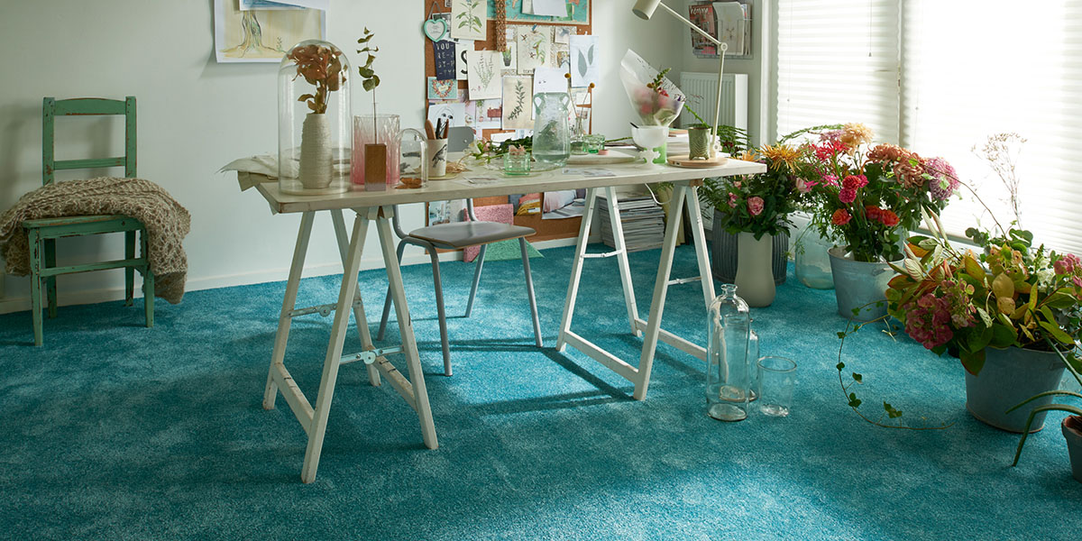 Ein blauer Teppichboden in einem Zimmer mit einem Tisch und Blumen. Firmenadresse