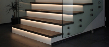 Eine Treppe mit Glasgeländer, LED-Leuchten und Produkten. Firmenadresse