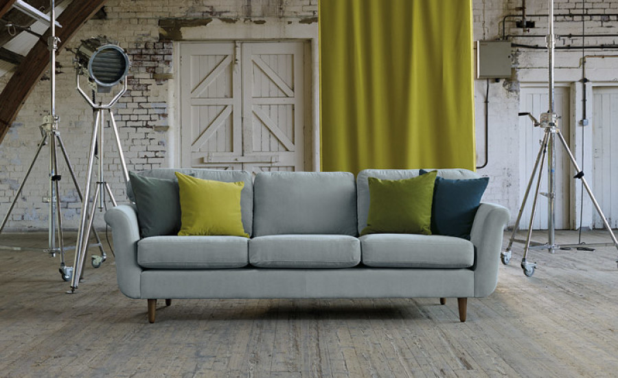 Bild Aufmaß Ein modernes Wohnzimmer-Set mit einer grauen Couch mit gelben und grünen Kissen und Studiobeleuchtung vor einer strukturierten weißen Ziegelwand mit drapiertem gelben Vorhang. Firmenadresse