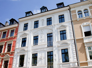 Eine Reihe mehrstöckiger Gebäude mit reich verzierten Fassaden, großen Fenstern und dekorativen architektonischen Elementen schimmerten unter dem klaren blauen Himmel, ähnlich wie eine Szene aus einem Gemälde von Maler Lauer. - Firmenadresse